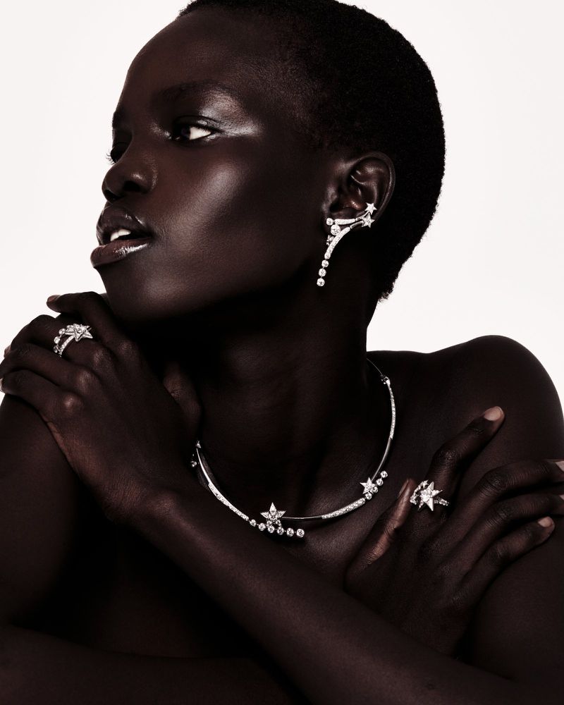 Close-up of an adult African female showcasing diamond jewelry: a necklace, rings, and earrings, set against a plain background.