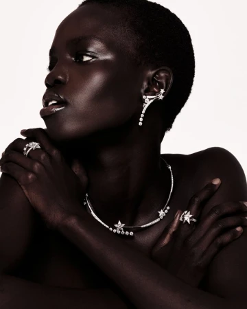 Close-up of an adult African female showcasing diamond jewelry: a necklace, rings, and earrings, set against a plain background.