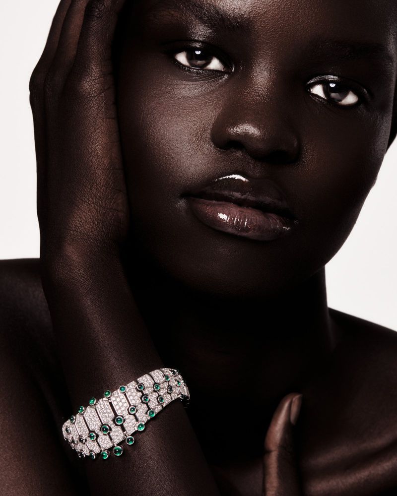 Close-up of a dark-skinned woman wearing a gemstone bracelet, hand near her face, against a plain backdrop. Beauty and fashion shot.