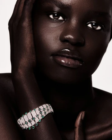 Close-up of a dark-skinned woman wearing a gemstone bracelet, hand near her face, against a plain backdrop. Beauty and fashion shot.