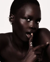 Close-up portrait of a model with short dark hair wearing diamond earrings and rings against a plain white background