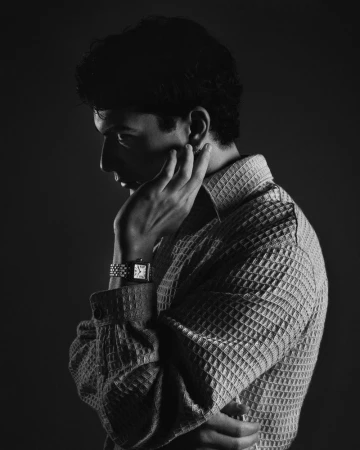 Monochrome portrait of a man in a textured shirt, hand near his face, wearing a watch, captured with soft, directional lighting.