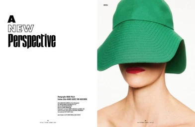 Close-up portrait of a model wearing a large green hat that covers the upper face, revealing bright red lips.