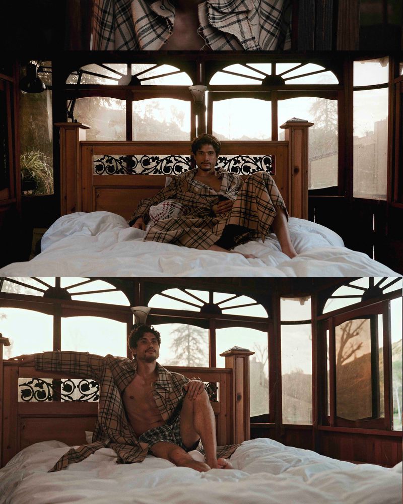 Man in plaid robe relaxing on bed with white sheets in a room with wooden frames, windows, and natural light coming in.