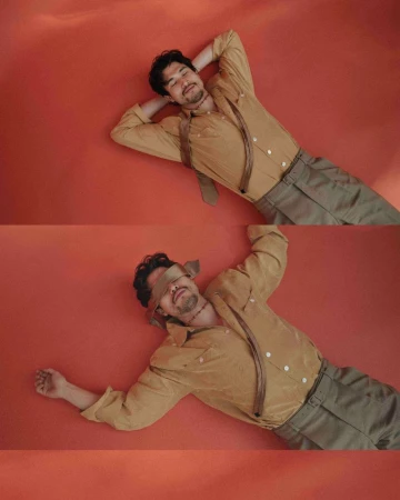 Man with blindfold and another view of him with head above hands, lying on orange background, wearing gold shirt and gray pants.