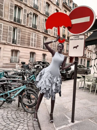 Woman in gray dress poses with red umbrella sign on Paris street surrounded by bicycles and architecture in a fashion editorial.