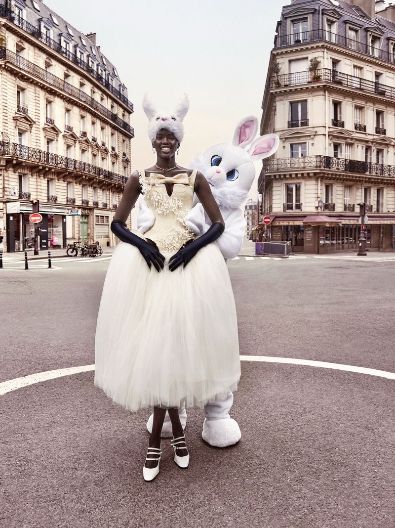 Fashion editorial shot in Paris featuring a Black woman wearing a ballgown and a furry rabbit headpiece next to a human-sized rabbit.