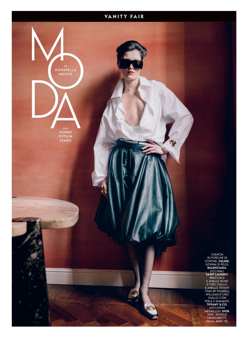 Editorial fashion shot of a female model wearing an oversized white shirt and black leather skirt against a textured terracotta background.