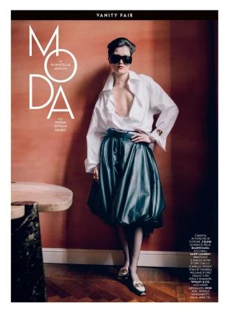 Editorial fashion shot of a female model wearing an oversized white shirt and black leather skirt against a textured terracotta background.