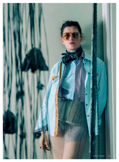 Fashion shot of a woman with sunglasses and a patterned outfit leaning against a wall with modern art for a high-end magazine.