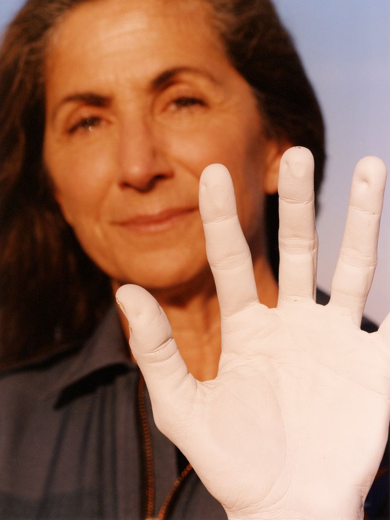 Close-up portrait of a woman holding up a white painted hand against a soft blurred background