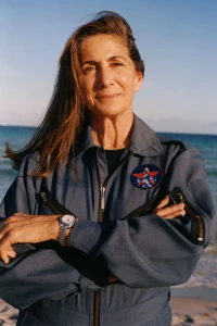 Mature woman in a blue jumpsuit with arms crossed on a sandy beach for Mastermind Magazine Out Of This World editorial.