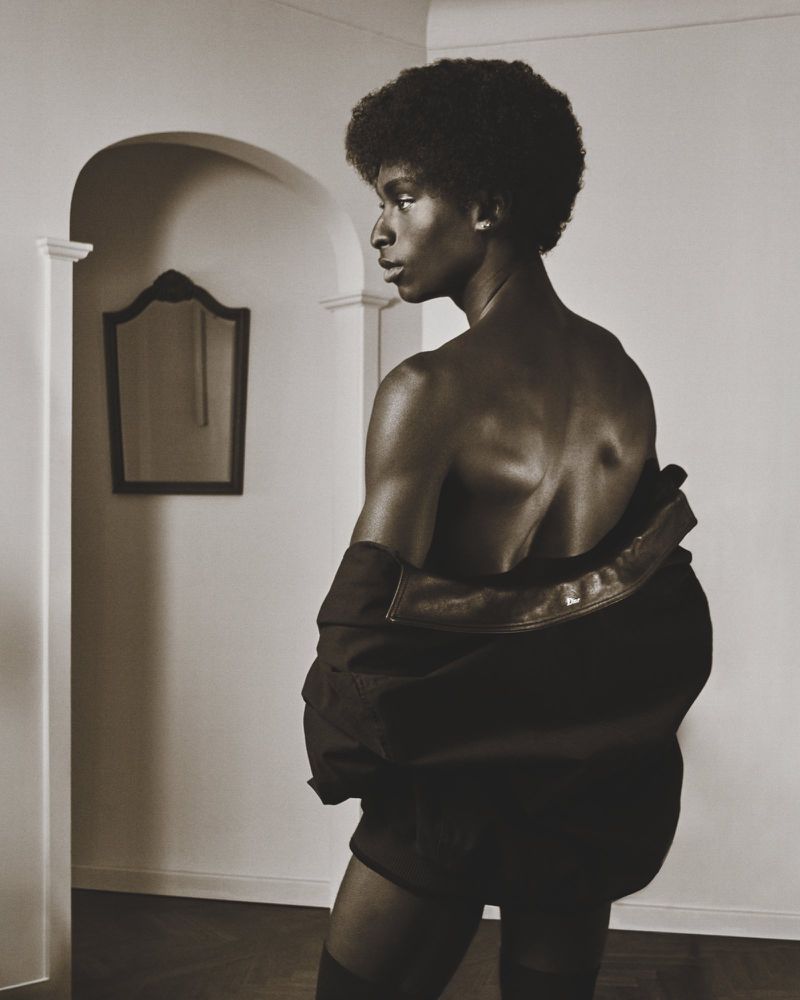 Striking portrait of a topless African American man with an afro, wearing a jacket, in an indoor setting with muted sepia tones.