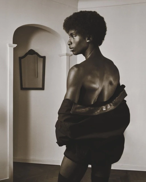 Striking portrait of a topless African American man with an afro, wearing a jacket, in an indoor setting with muted sepia tones.