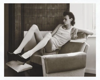 Model wearing a white tank top and black high heels seated in an armchair for an editorial feature in Numero Netherlands.