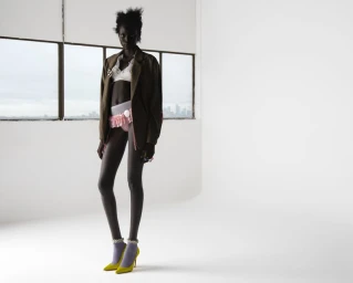 Model Aluel Keror in oversized brown blazer, white bralette, and ruffled shorts standing against a white backdrop.