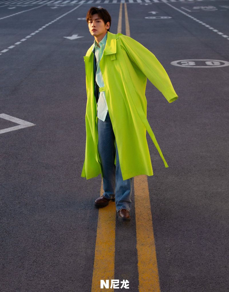 Stylish adult male in a neon green coat stands on an urban road with painted lane lines, captured in a fashion-forward outdoor portrait.