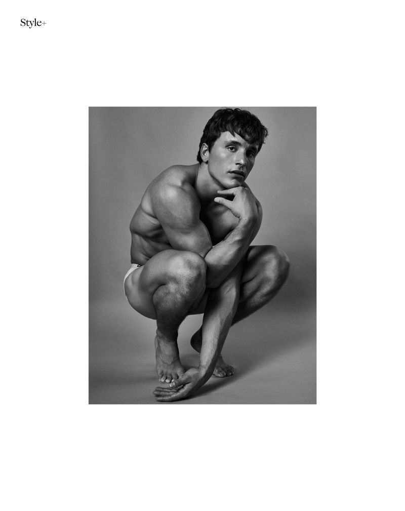 Monochrome studio shot of a muscular adult male crouched with hand on chin. The image features clean lines, neutral tones, and focus on form.