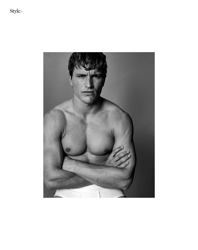 Portrait of a shirtless man with folded arms wearing white underwear against a grey studio backdrop for The Perfect Man Magazine.