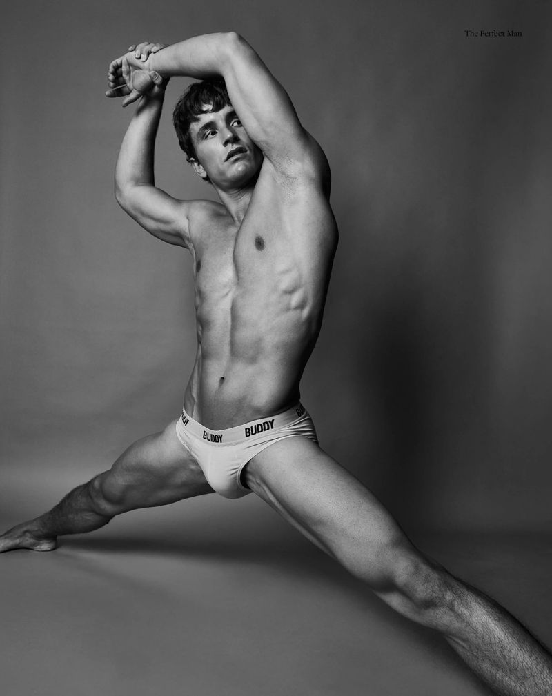 Athletic man in briefs strikes a dynamic pose against a neutral backdrop, showcasing musculature and flexibility in black and white.