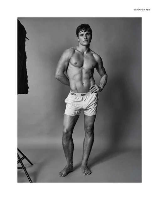Black and white studio portrait of a muscular adult man in underwear, standing barefoot with his hands on his hips.