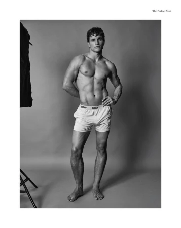 Black and white studio portrait of a muscular adult man in underwear, standing barefoot with his hands on his hips.