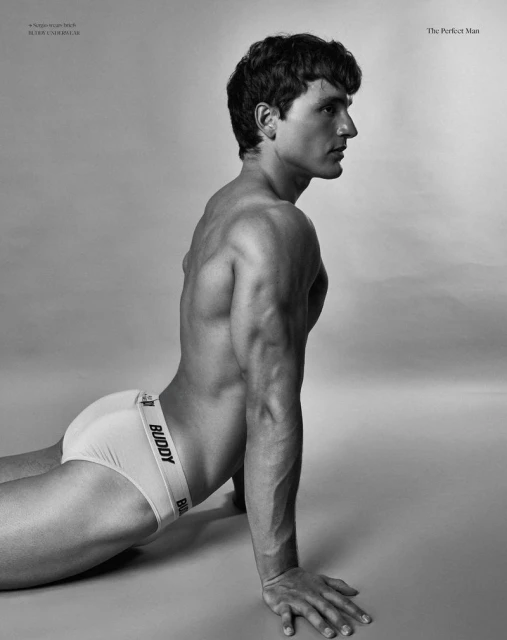 Black and white portrait of an adult male with visible muscles posing in underwear against a neutral background.