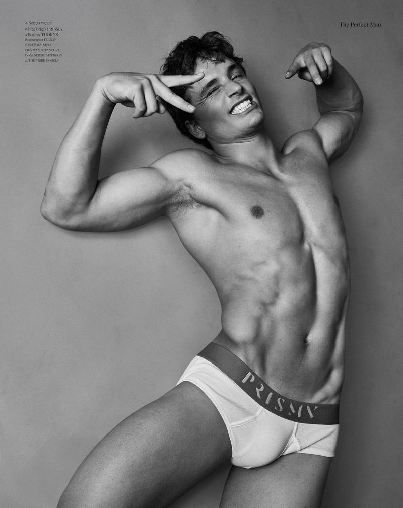 Monochrome fashion portrait of a shirtless male model wearing branded briefs in a studio setting.