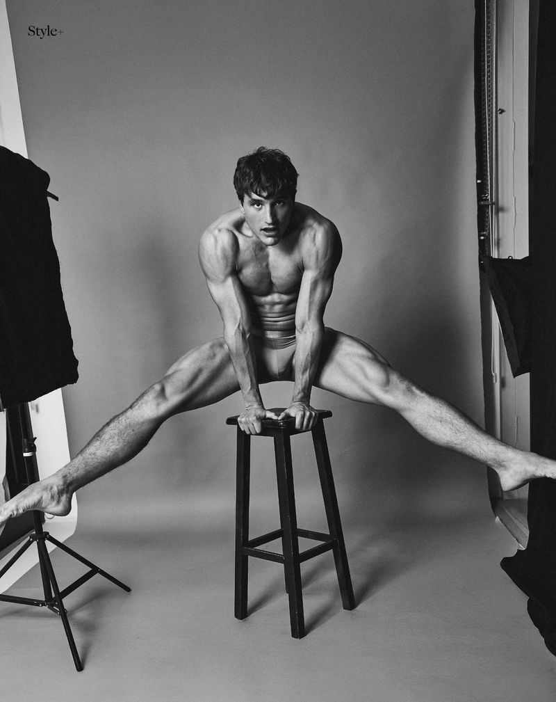 Striking black and white portrait of a muscular man balancing on a stool in a studio, showcasing fitness and strength.