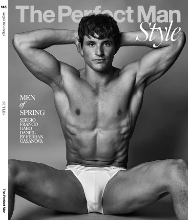 Shirtless male model seated with hands behind head wearing white briefs against a plain grey backdrop for a magazine cover.
