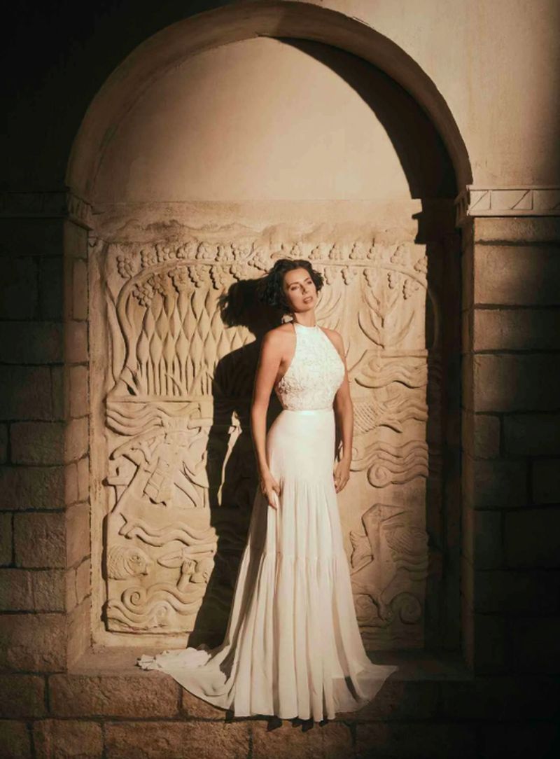 Elegant woman in a white gown poses in an arched stone doorway with carved designs in a warm, low-light setting. 