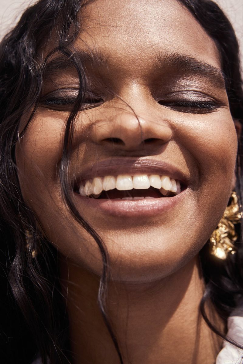 Close-up portrait of smiling woman wearing gold earrings with dark hair blowing across face for H&M Cape Town campaign