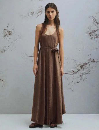 Model wearing a brown maxi dress with a waist tie standing against a mottled marble texture wall for Marella Monochrome S/S 2026