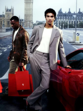 Two men with shopping bags stand near a red Ferrari in front of the Houses of Parliament in London, wearing fashionable suits.