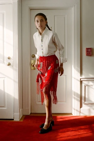 Woman in vintage fashion posing in an indoor setting with a white blouse and a red fringe skirt with white doors in the background.