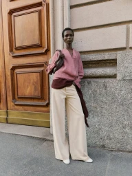 Model Amar Akway in mauve linen top and wide trousers standing outdoors against a carved wooden door and stone wall