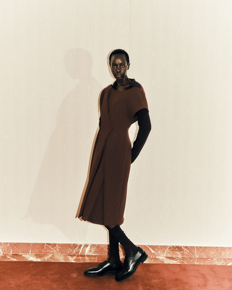A single Black female fashion model poses in a brown dress against a neutral background in a studio setting, showcasing an editorial style.