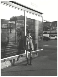 Model standing outdoors next to a large glass storefront window wearing a jacket and knee-high socks