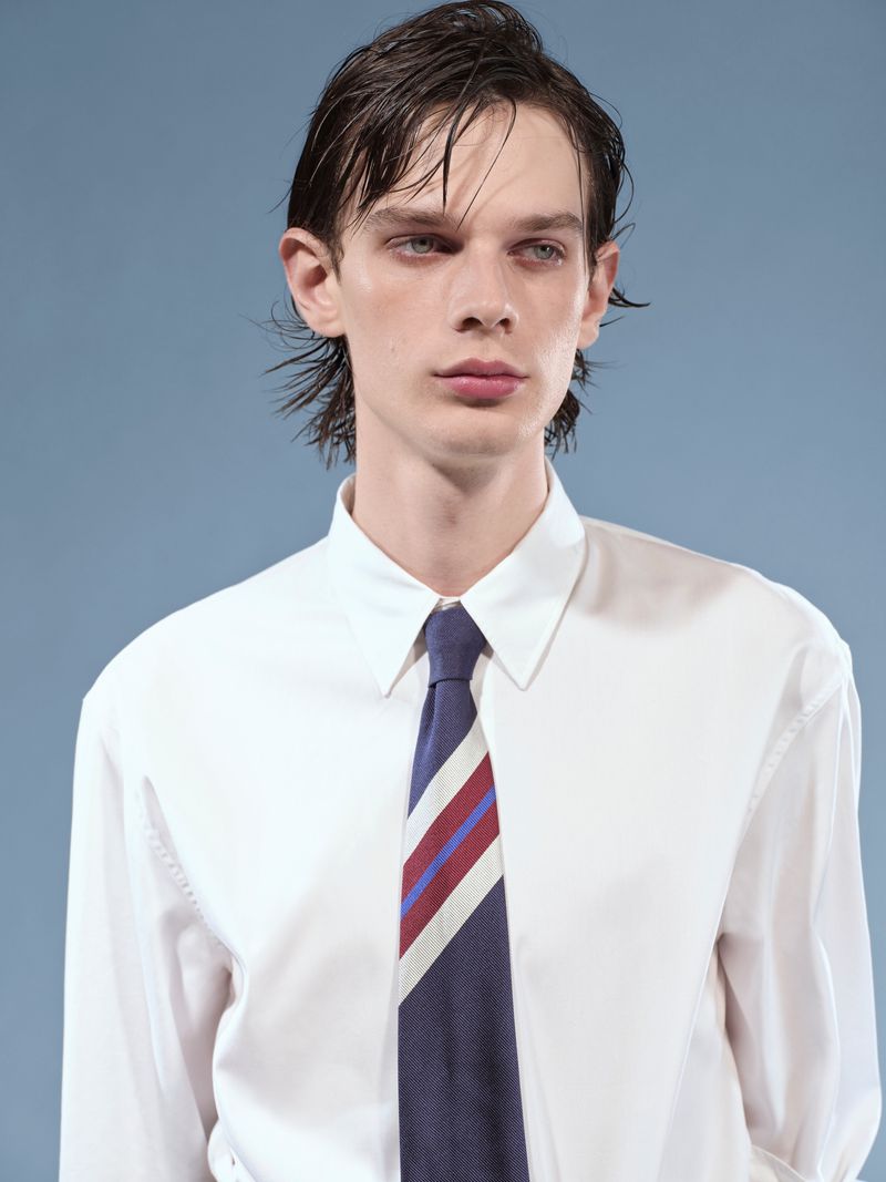 Close-up of a young adult man in a white shirt and striped tie against a light blue backdrop, showcasing a fashion-forward aesthetic.