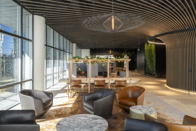 Interior space with lounge chairs arranged on a patterned rug, tables, and a long table with chairs in a modern office setting.