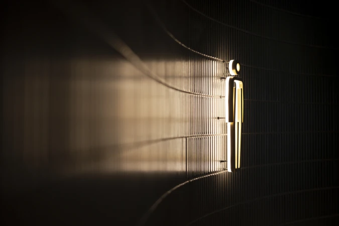 Illuminated man icon on textured wall. Simple, modern design with warm lighting in an indoor setting. Close-up shot with a focus on details.