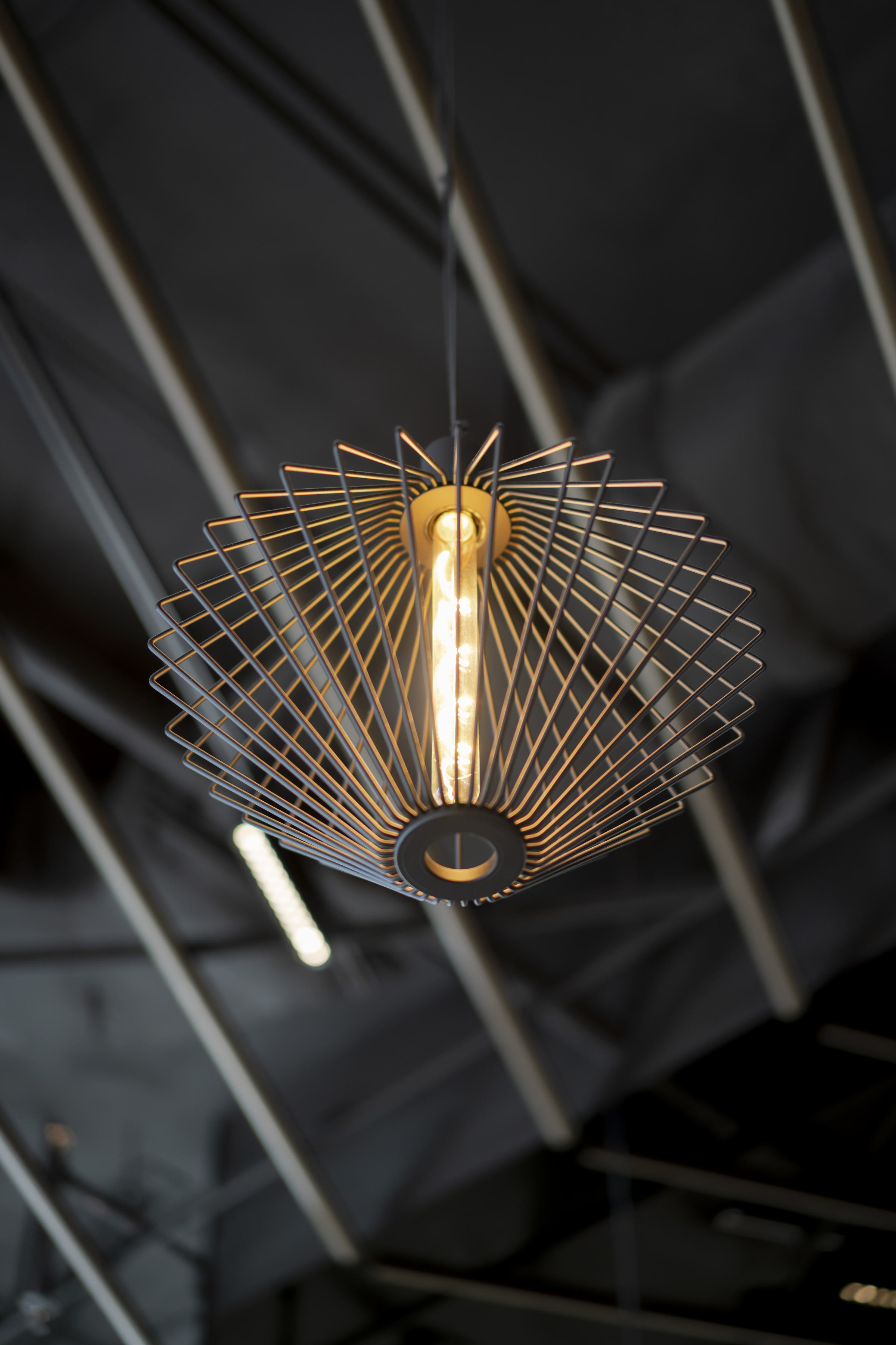 Geometric metal wire-frame pendant light fixture with an exposed edison bulb hanging indoors against a dark grey ceiling.