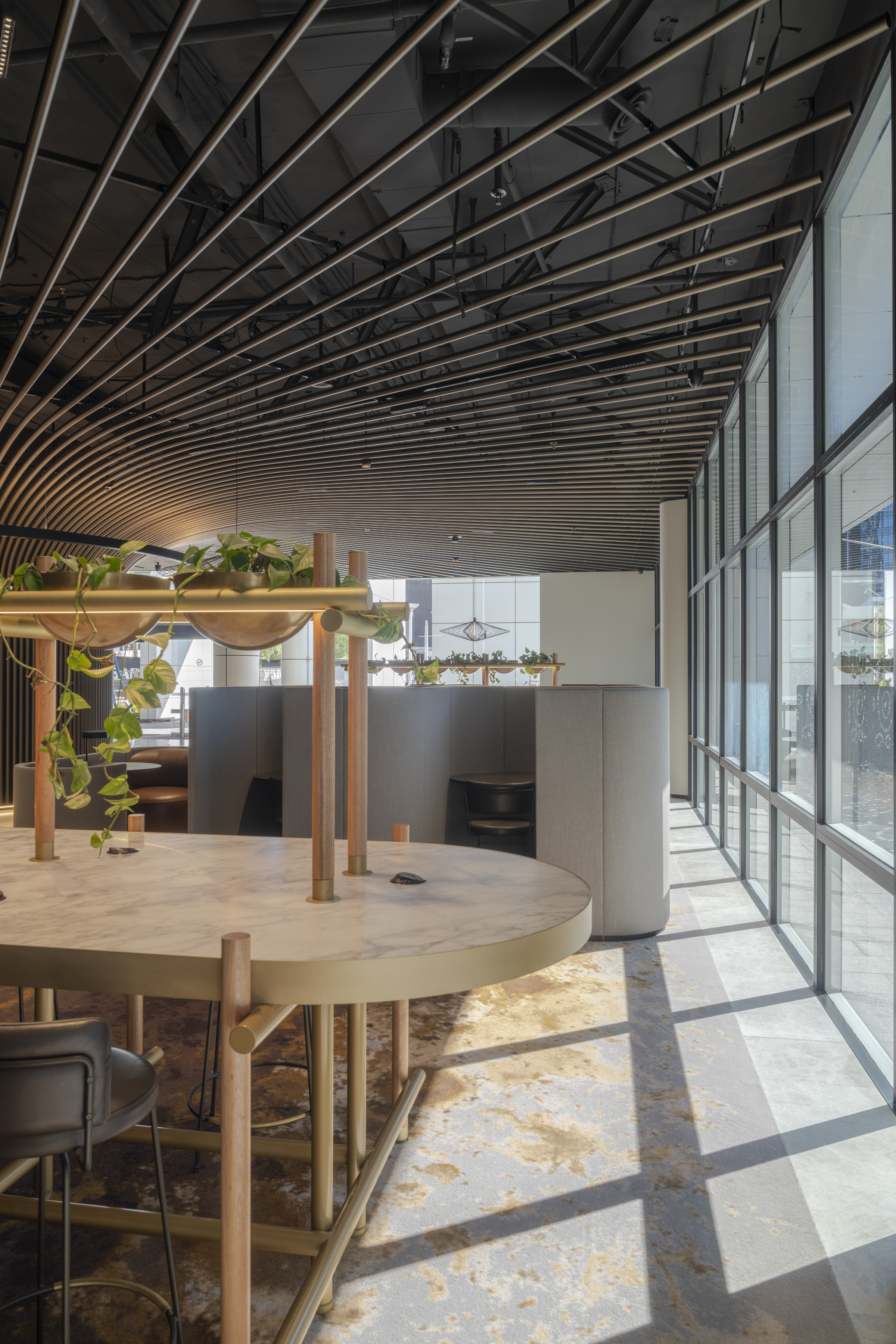 Modern office space featuring an open desk, a black ceiling with gold pipe accents, and a wall of windows providing natural light.