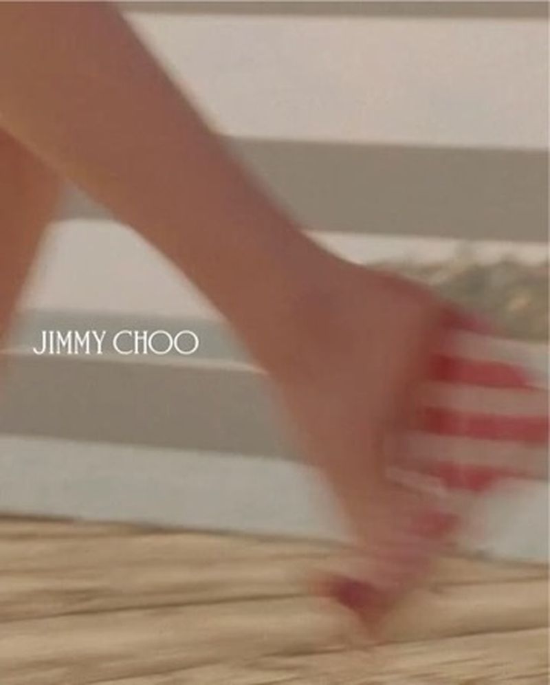 Bare feet walking on a striped surface next to a Jimmy Choo logo, suggesting a fashion theme or advertisement for a luxury brand.