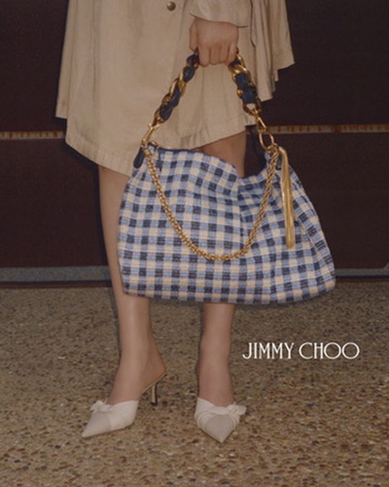 Fashion shot of a woman holding a blue and white checkered handbag with chain straps, paired with cream-colored high-heeled shoes.