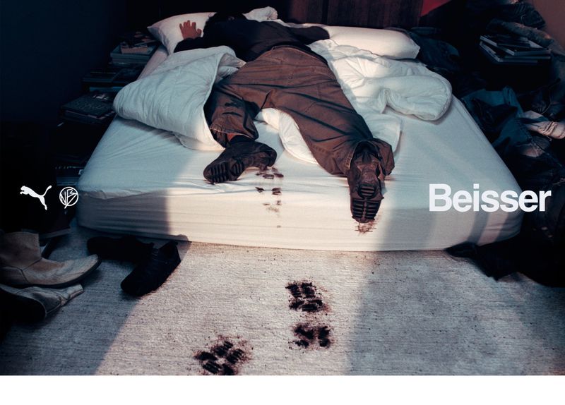 Person wearing brown pants and black boots lying on a white bed with dirt marks, with dirt footsteps visible on the carpet.
