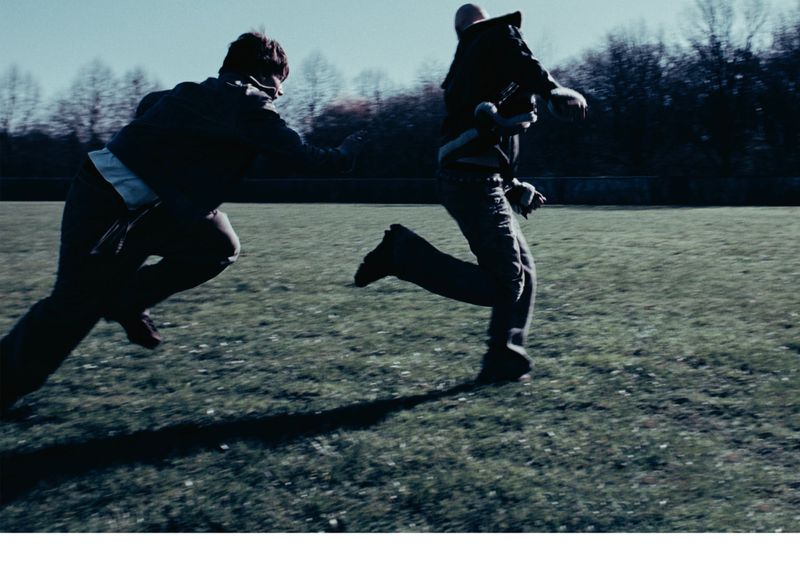 Two people running across a grassy field with trees in the background, motion blur, full shot.