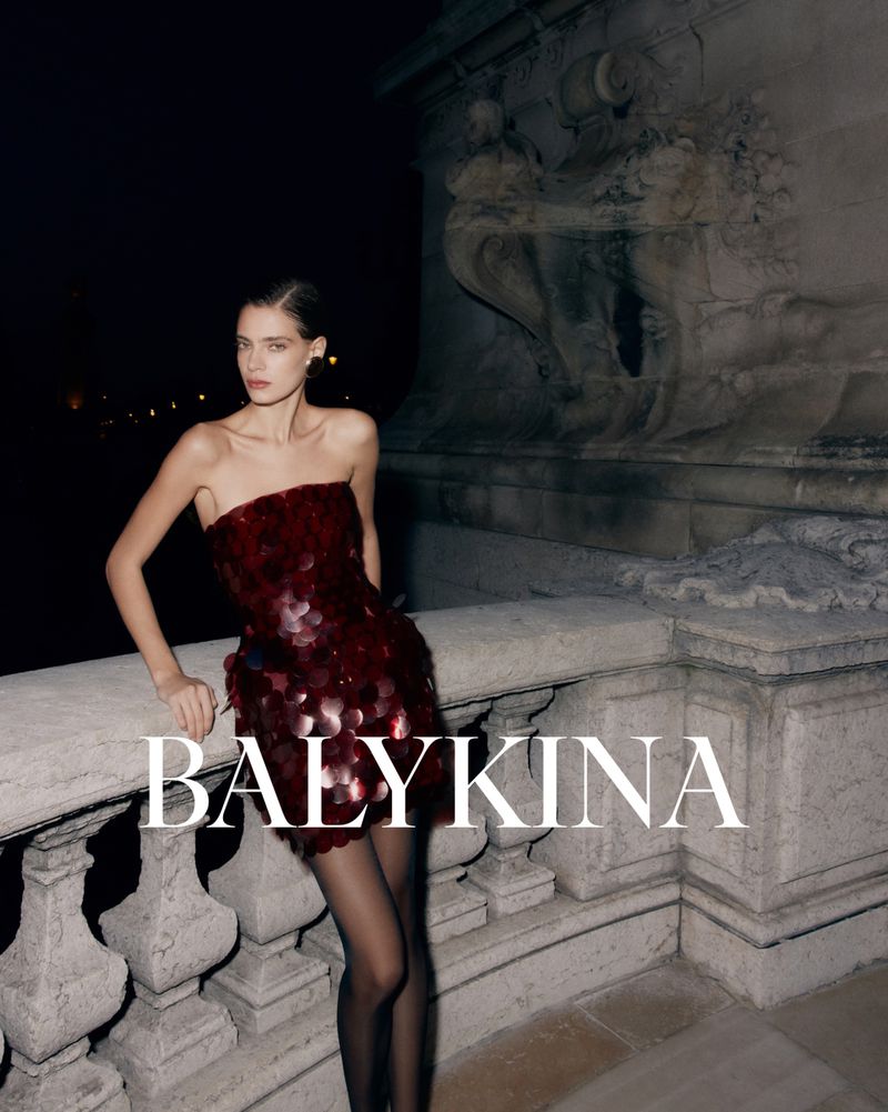 Elegant woman in a red strapless sequin dress and black stockings poses against a stone structure at night, showcasing fashion and style.