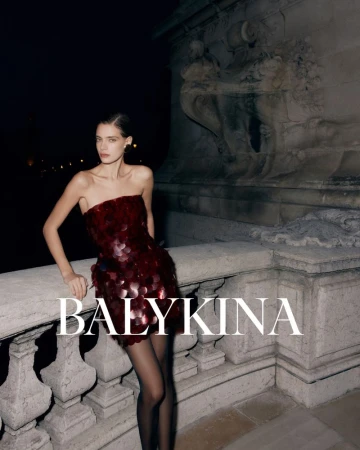 Elegant woman in a red strapless sequin dress and black stockings poses against a stone structure at night, showcasing fashion and style.