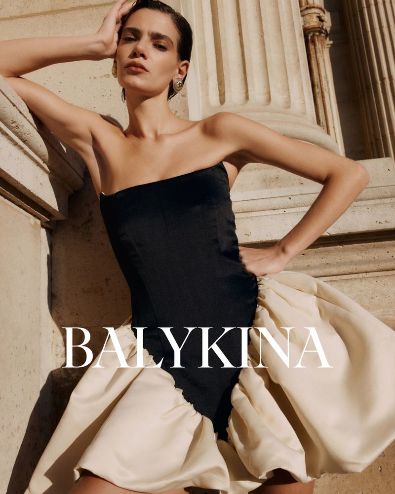 A woman poses in an elegant black and white strapless dress by a light stone pillar, showcasing a fashion-forward style for Visie.